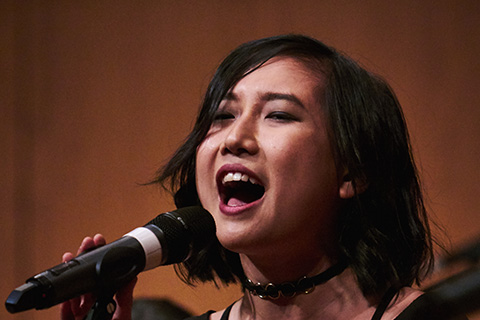 Dark haired woman singing into a microphone