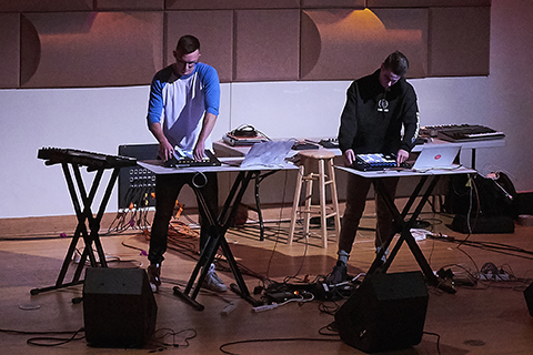 Two men with drum machines perform on stage during an event